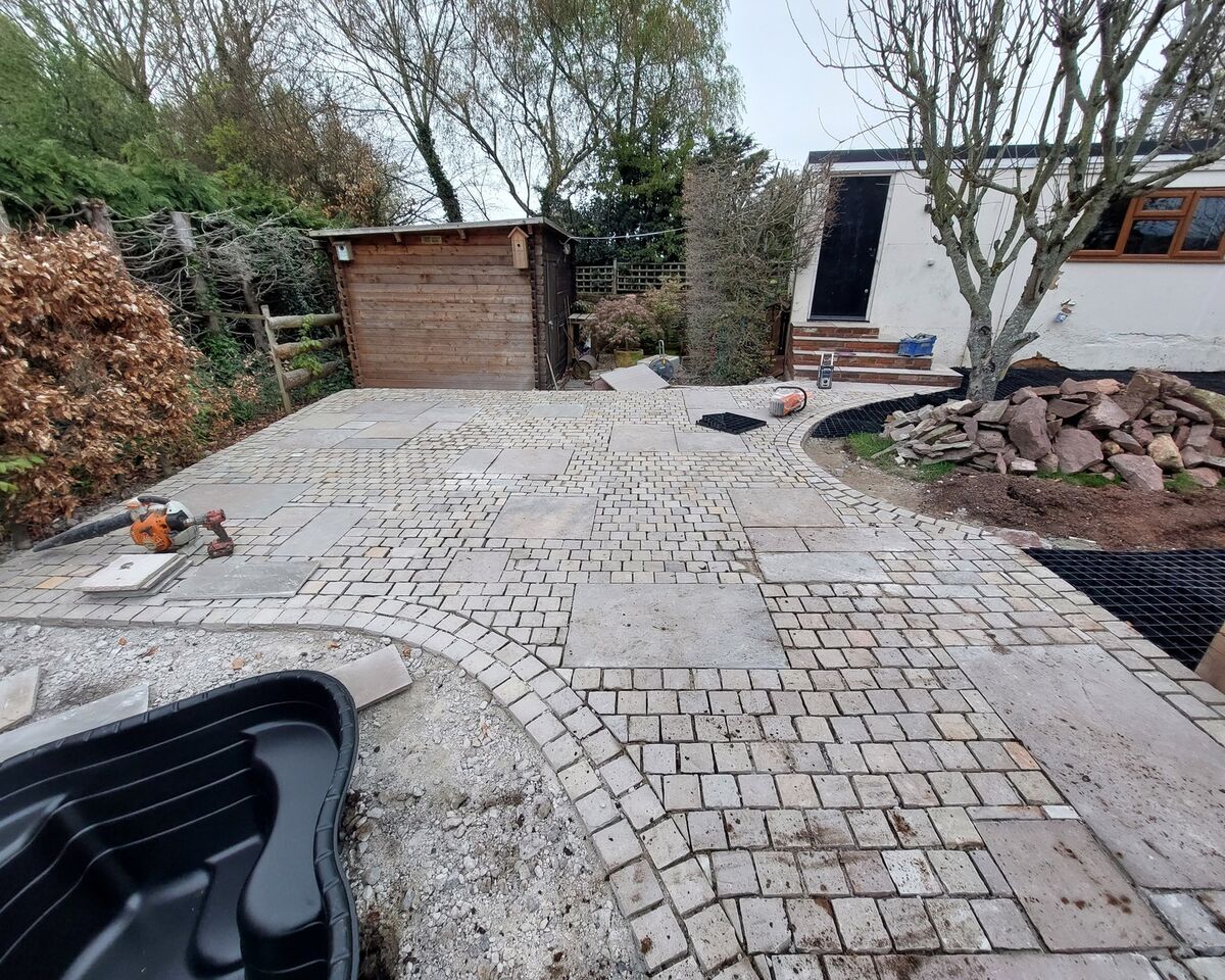 Patio area with stone paving, a storage shed, and a house in the background.