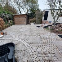 Patio area with stone paving, a storage shed, and a house in the background.