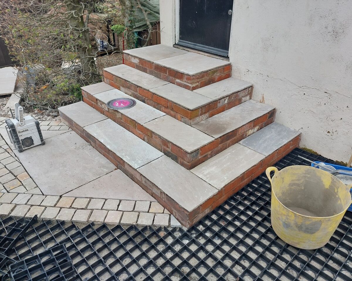 Steps made of stone tiles leading to a door, with a yellow bucket nearby.