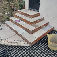 Steps made of stone tiles leading to a door, with a yellow bucket nearby.