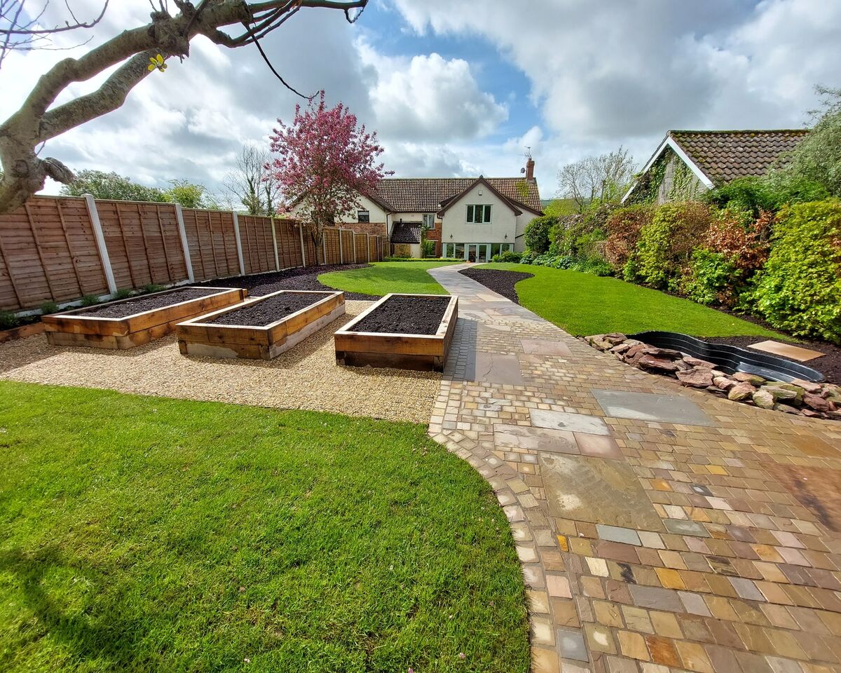 A landscaped garden with raised planters, a stone path, and a house in the background.