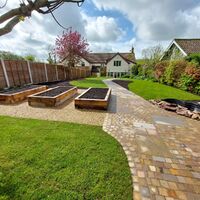 A landscaped garden with raised planters, a stone path, and a house in the background.