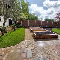 A garden with raised wooden beds, grassy areas, and a stone pathway under a cloudy sky.