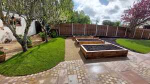 Garden with raised planter beds, green grass, and trees under a cloudy sky.