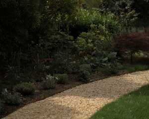 Gravel path curving past a deep mixed border with a Japanese maple and metal arch