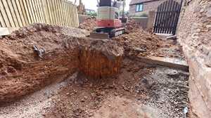 Mini digger excavating a deep drainage trench along a fence line in clay ground