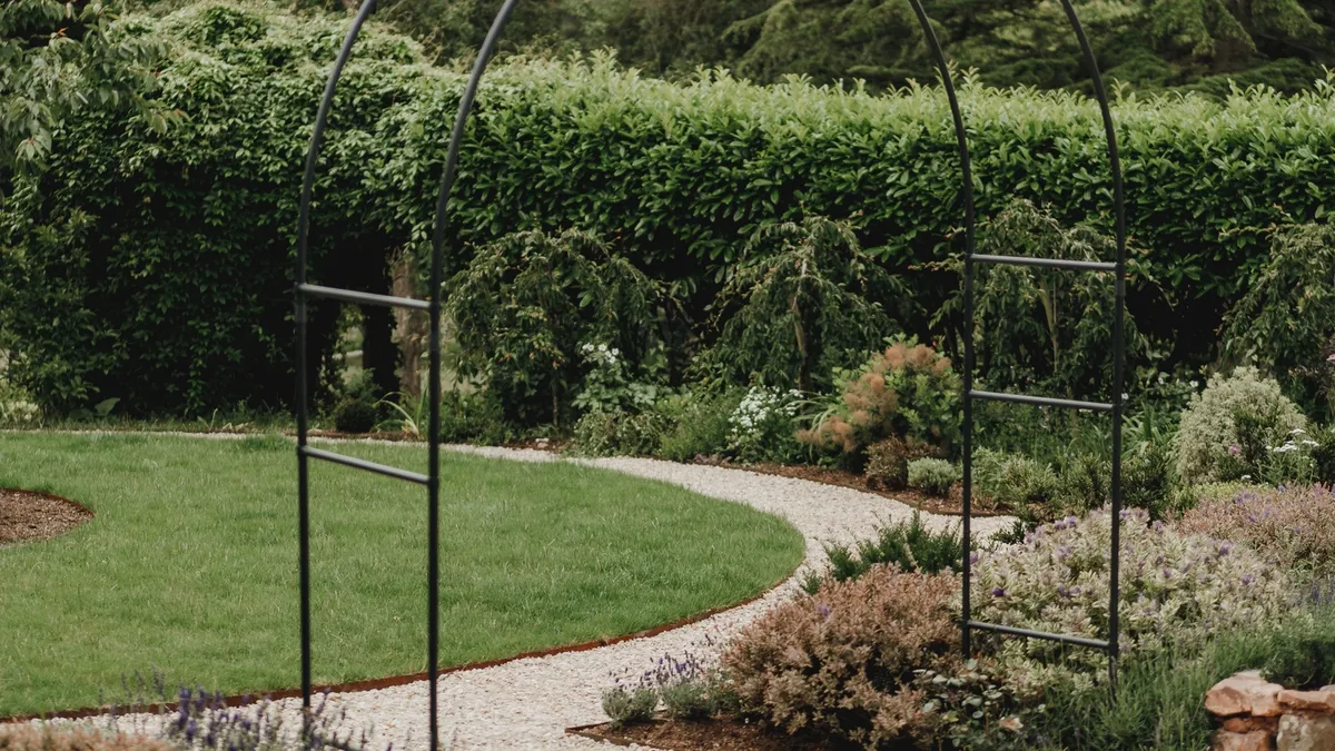Metal arch over the gravel path, with the circular lawn and stone-edged bed behind