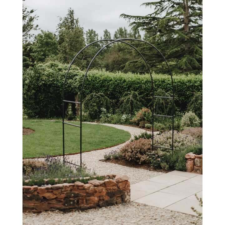 Metal arch over the gravel path, with the circular lawn and stone-edged bed behind