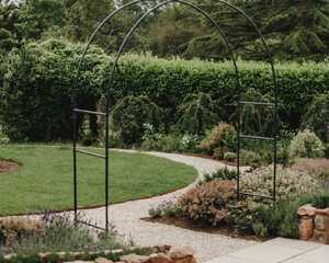 Metal arch over the gravel path, with the circular lawn and stone-edged bed behind