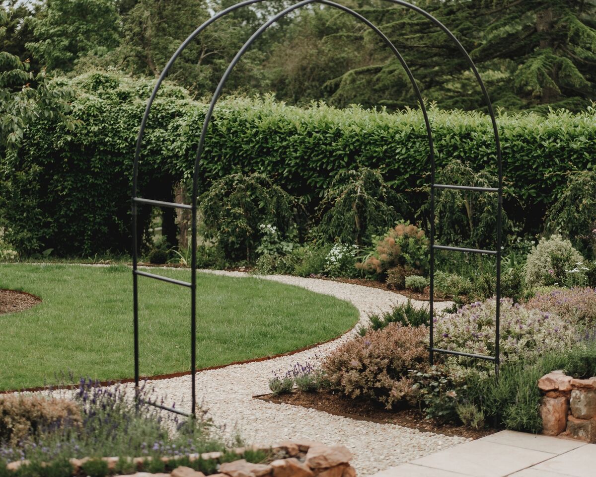 Metal arch over the gravel path, with the circular lawn and stone-edged bed behind