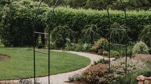 Metal arch over the gravel path, with the circular lawn and stone-edged bed behind