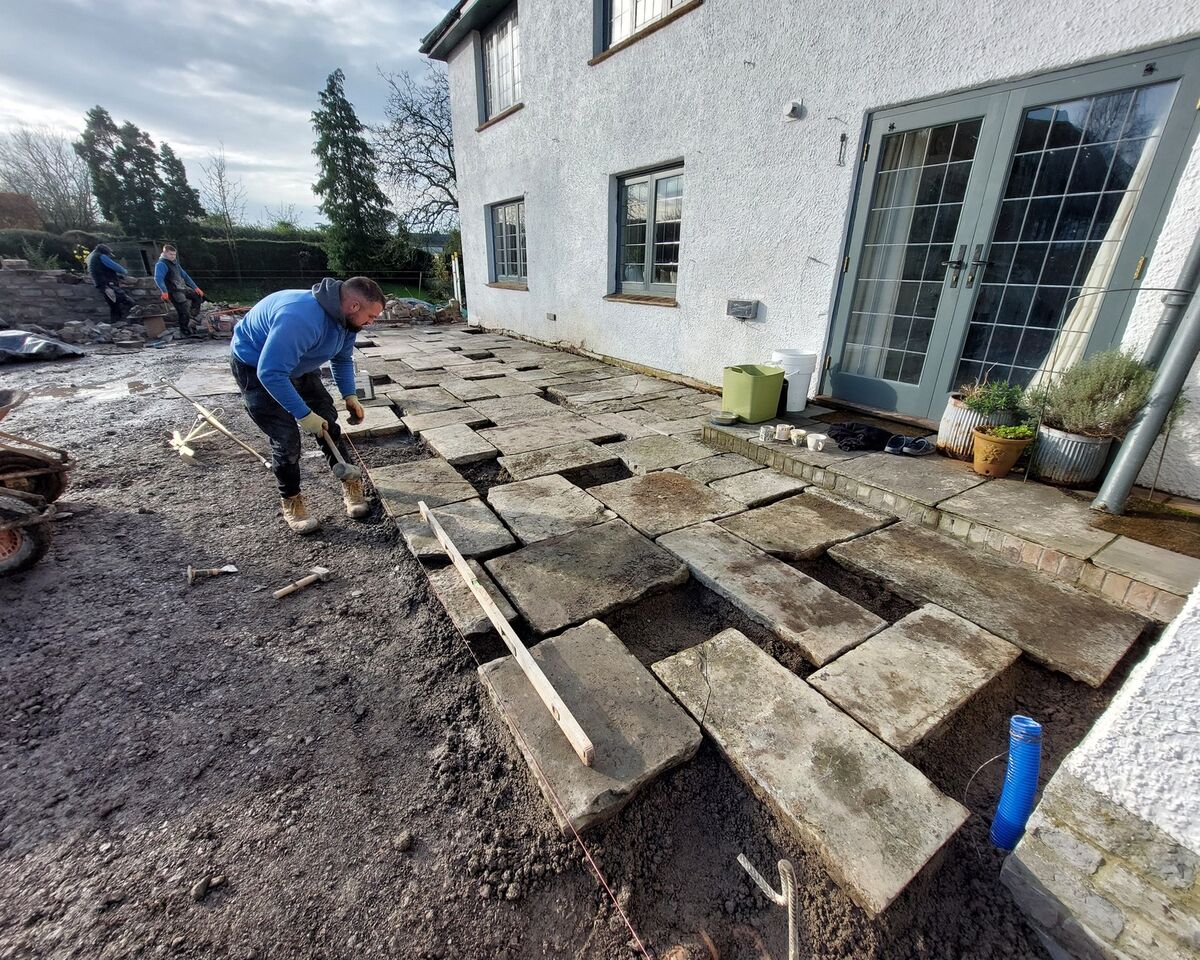 Person installing paving stones outside a house, with some stones unevenly placed.