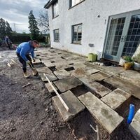 Person installing paving stones outside a house, with some stones unevenly placed.