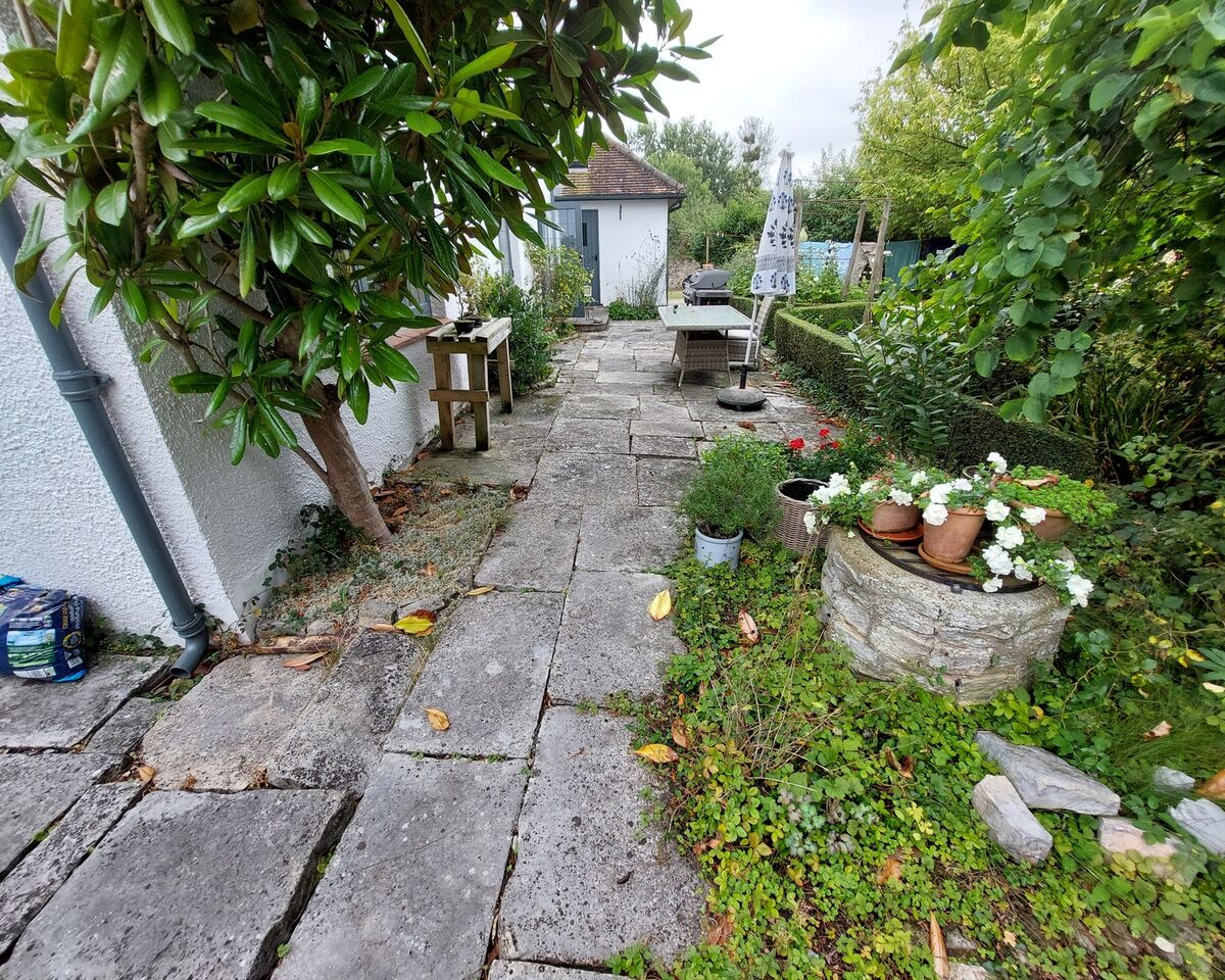 A stone pathway through a lush garden with plants and decorative pots.
