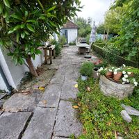 A stone pathway through a lush garden with plants and decorative pots.