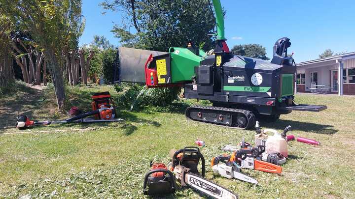 A glass greenhouse with plants, adjacent to a stone path and house, under a cloudy sky.