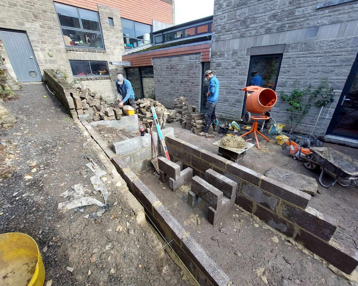 Construction area with workers, stone walls, and equipment in a narrow outdoor space.