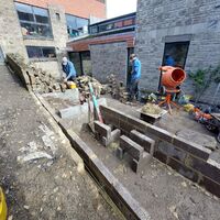 Construction area with workers, stone walls, and equipment in a narrow outdoor space.