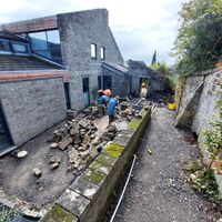 Construction site with workers and stone materials beside a modern building.