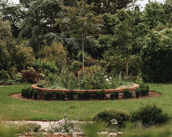 Brick-edged circular planting bed set into the lawn at the centre of the formal garden