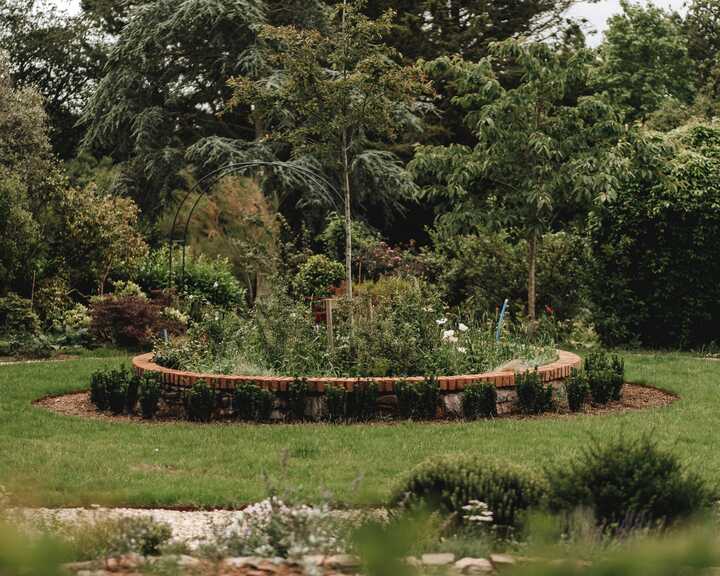 Brick-edged circular planting bed set into the lawn at the centre of the formal garden