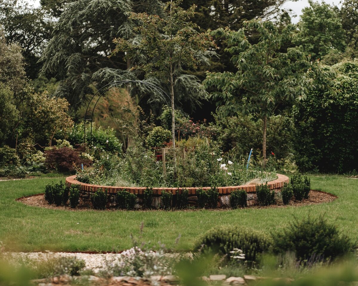 Brick-edged circular planting bed set into the lawn at the centre of the formal garden