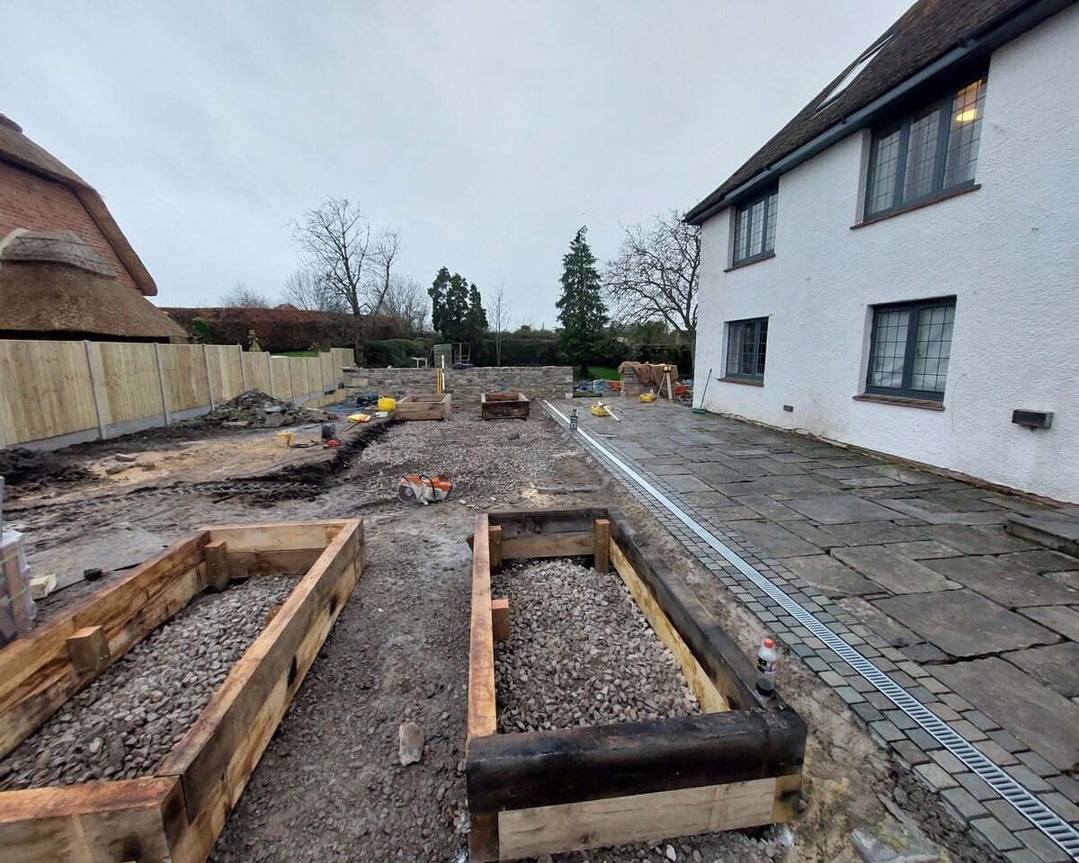 Construction site with wooden frames and a partially cleared area beside a white house.