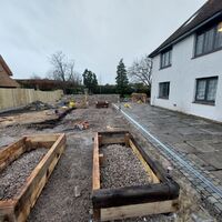 Construction site with wooden frames and a partially cleared area beside a white house.