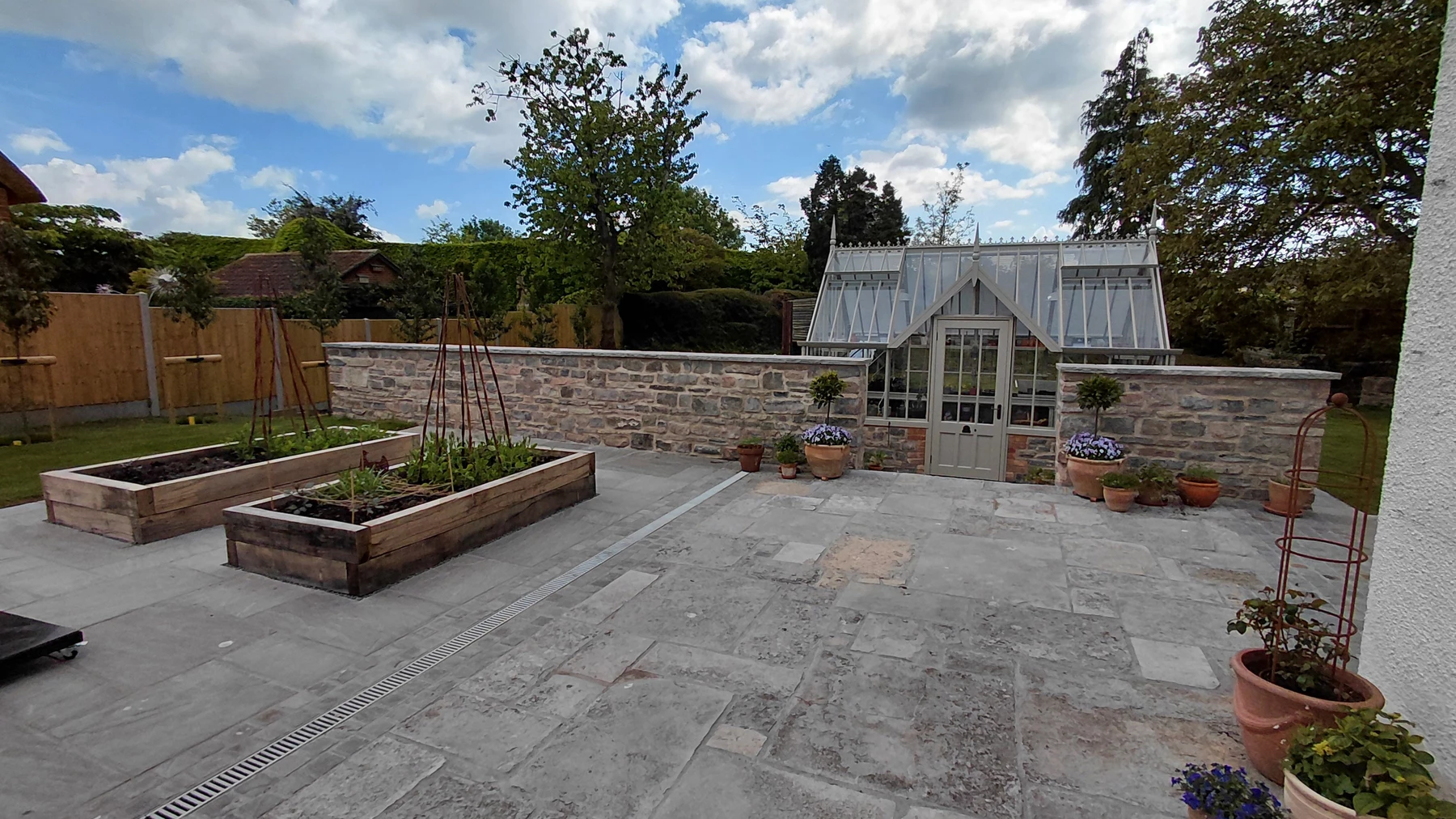 Raised vegetable beds and reclaimed stone paving leading to the greenhouse entrance