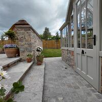 Garden setting with a stone wall, patio steps, and a greenhouse under a cloudy sky.