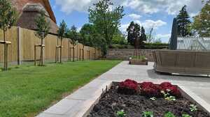 New lawn, paved terrace and raised planting beds bordered by a reclaimed stone wall, with the greenhouse beyond