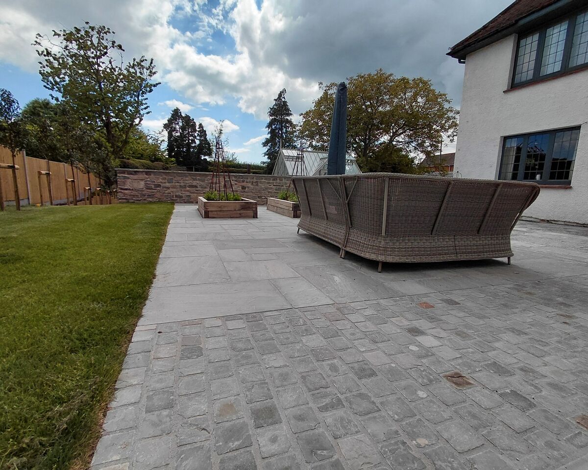 Outdoor patio with seating, lawn, and house in the background under a cloudy sky.
