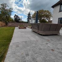 Outdoor patio with seating, lawn, and house in the background under a cloudy sky.