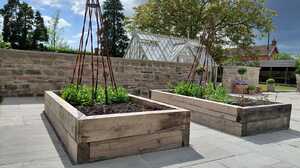 Timber raised beds with plant supports on a reclaimed stone terrace, greenhouse and stone walls in the background