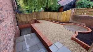 A landscaped outdoor area with gravel, bricks, and a wooden fence.