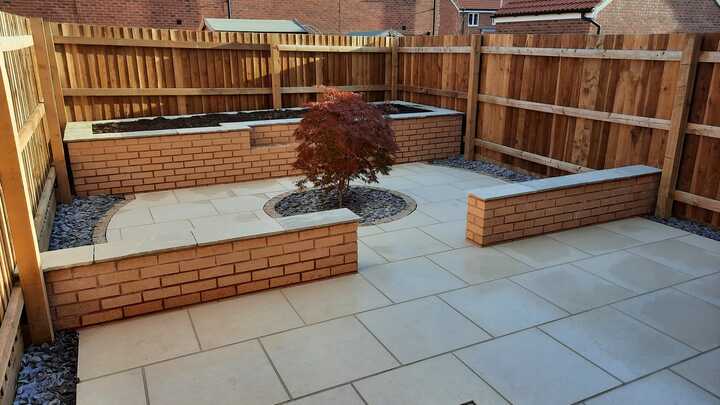 A glass greenhouse with plants, adjacent to a stone path and house, under a cloudy sky.
