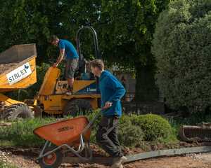 Sibley Landscapes dumper unloading while a team member barrows material to the new beds
