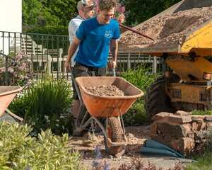 Team members moving gravel by wheelbarrow from the dumper beside the house