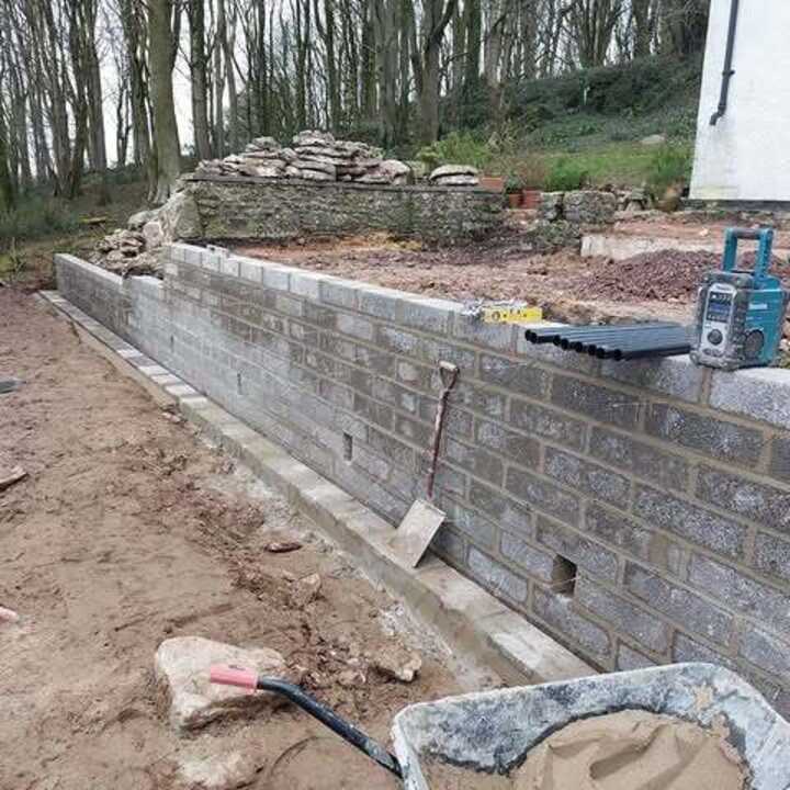 Construction site with a stone wall, tools, and equipment in a wooded area.