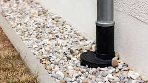 Downpipe running into a gully set in a gravel drainage bed beside a house wall