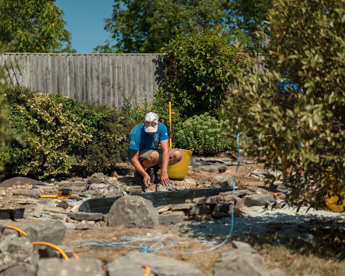 Team member building up the rockery around the pond with a hose and buckets nearby