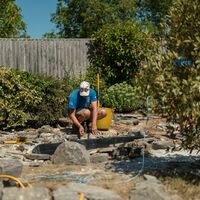 Team member building up the rockery around the pond with a hose and buckets nearby
