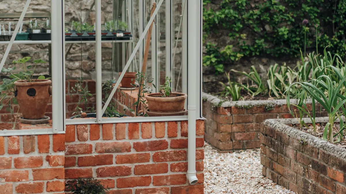 Pale stone paving and gravel border laid around the corner of the greenhouse