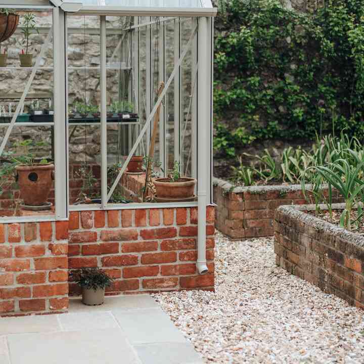 Pale stone paving and gravel border around the greenhouse corner