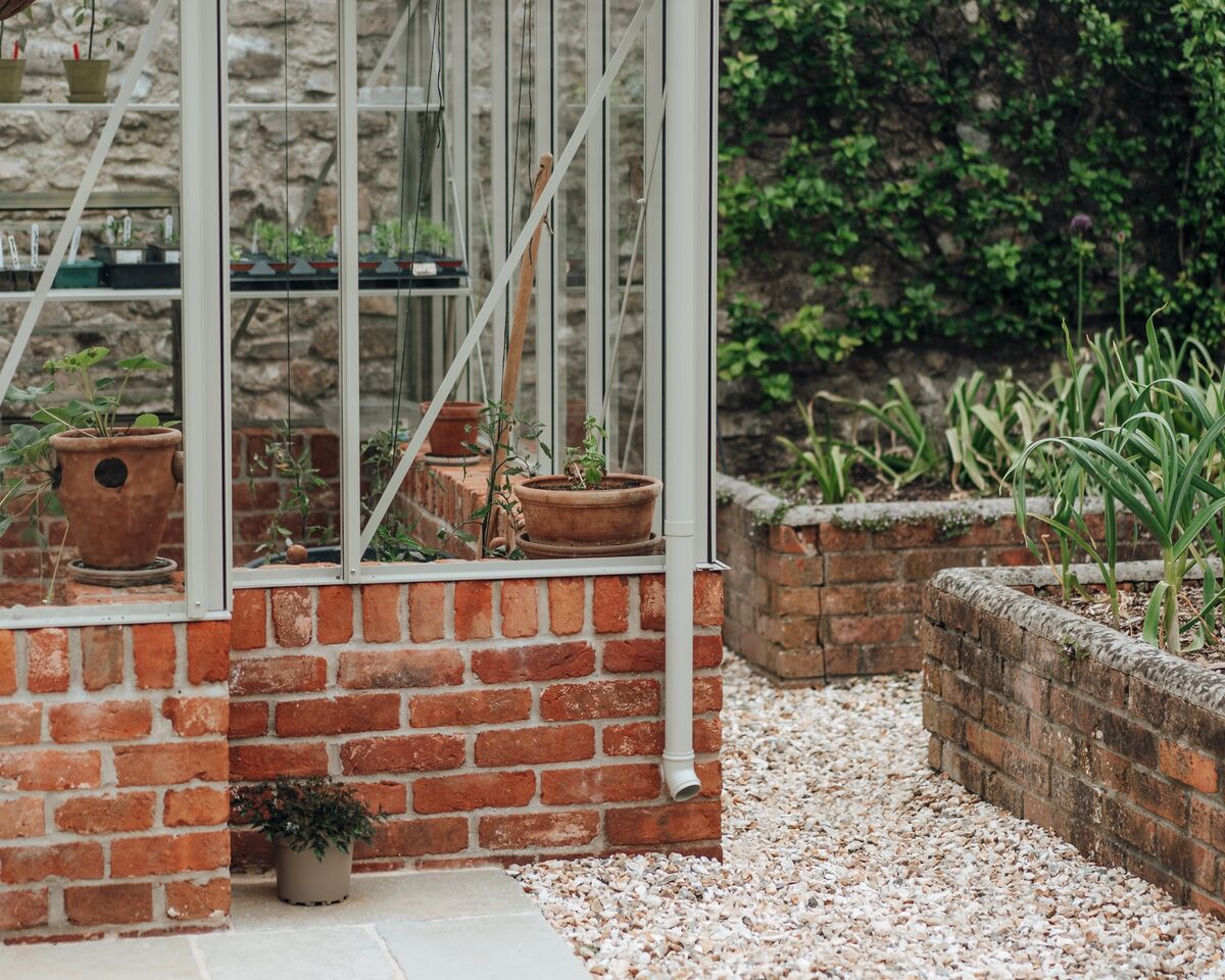 Pale stone paving and gravel border around the greenhouse corner