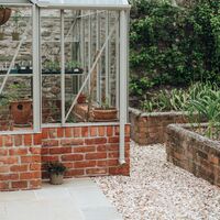 Pale stone paving and gravel border around the greenhouse corner