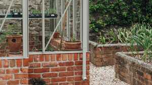 Pale stone paving and gravel border laid around the corner of the greenhouse