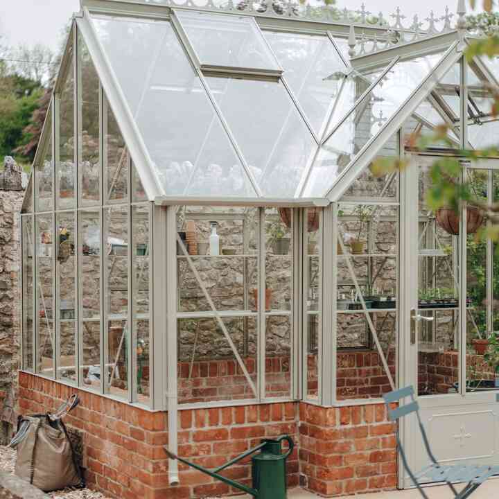 Heritage-style greenhouse with decorative roof cresting on a red brick plinth
