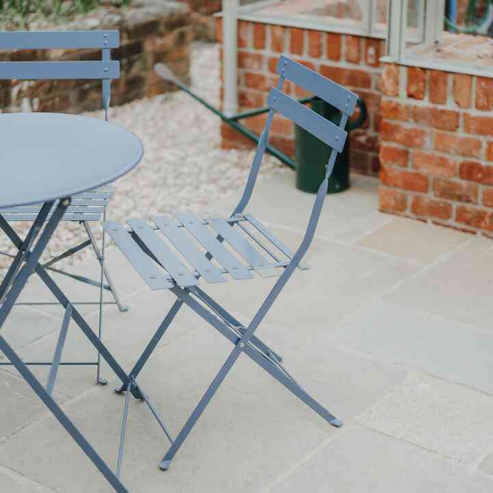 Blue bistro table and chairs on the paving beside the greenhouse