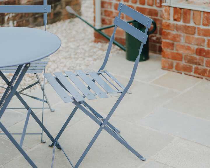 Blue bistro table and chairs on the paving beside the greenhouse